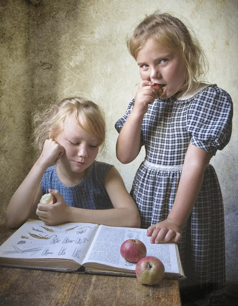Two girls eating apples while studying a book