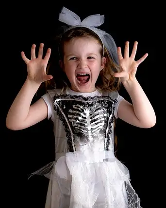 Little girl with hands up, being scary, and dressed like a princess with a skeleton chest. She is growling, and has a ribbon in her hair.
