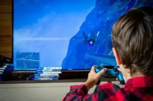 The back of a boys head can be seen as he stares at a TV screen, with game controllers in hand, playing a video game.