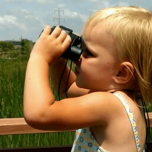 Little girl of 3 years explores the horizon with her benoculars