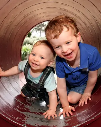 Two boys, aged 2 and 4 are happily crawling through a playground tunnel.