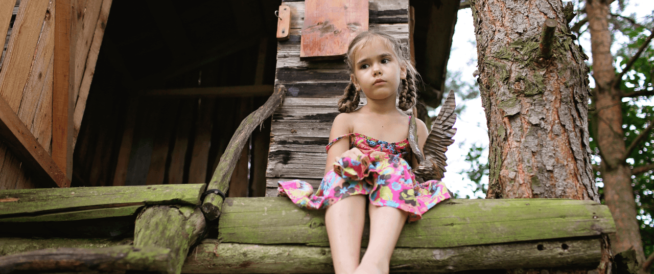 A young girl of about 7 years old, sits in a treehouse alone.