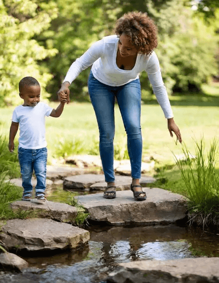 A Mom helps her young son navigate his steps on stones crossing a stream